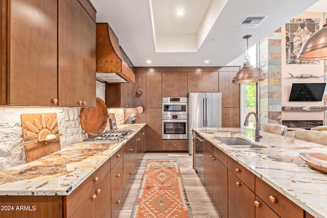 kitchen featuring custom exhaust hood, sink, hanging light fixtures, appliances with stainless steel finishes, and light hardwood / wood-style floors