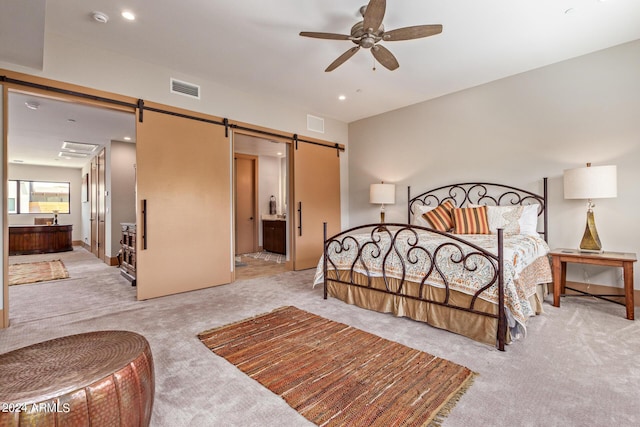 carpeted bedroom with a barn door, ensuite bathroom, and ceiling fan