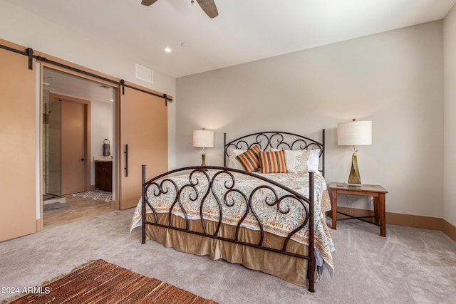 bedroom featuring ceiling fan, a barn door, light carpet, and connected bathroom