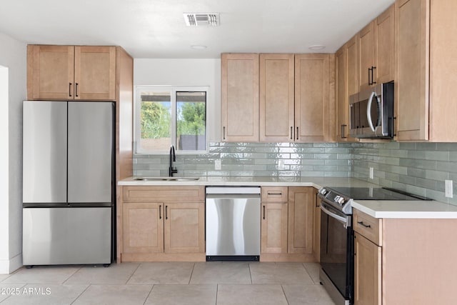 kitchen featuring stainless steel appliances, a sink, light brown cabinets, light countertops, and tasteful backsplash