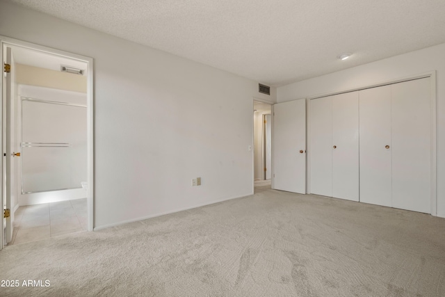 unfurnished bedroom with a closet, visible vents, light carpet, connected bathroom, and a textured ceiling