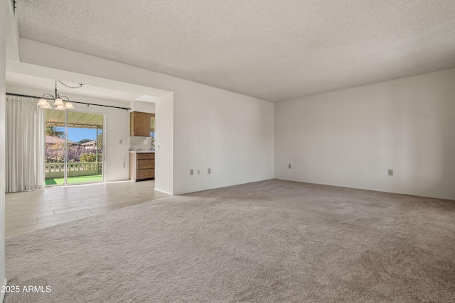 empty room with a chandelier, light colored carpet, and a textured ceiling