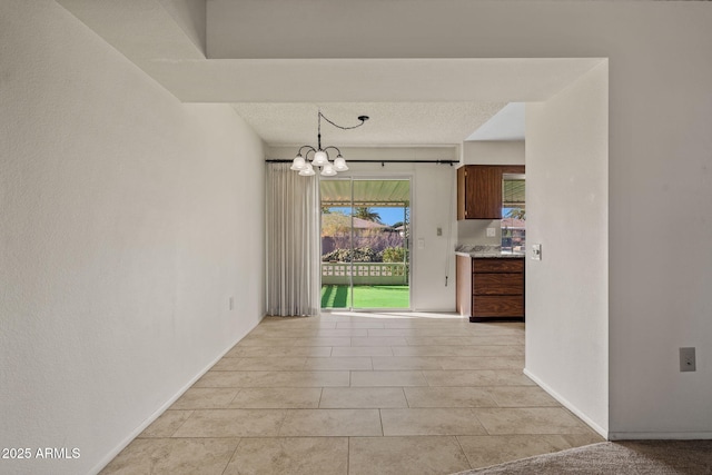 empty room with baseboards, light tile patterned floors, a textured ceiling, and an inviting chandelier