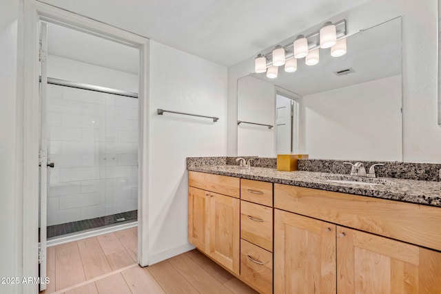 bathroom with double vanity, a stall shower, visible vents, wood finished floors, and a sink