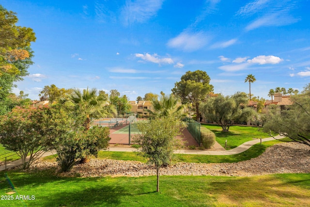 view of property's community with a tennis court, a lawn, and fence