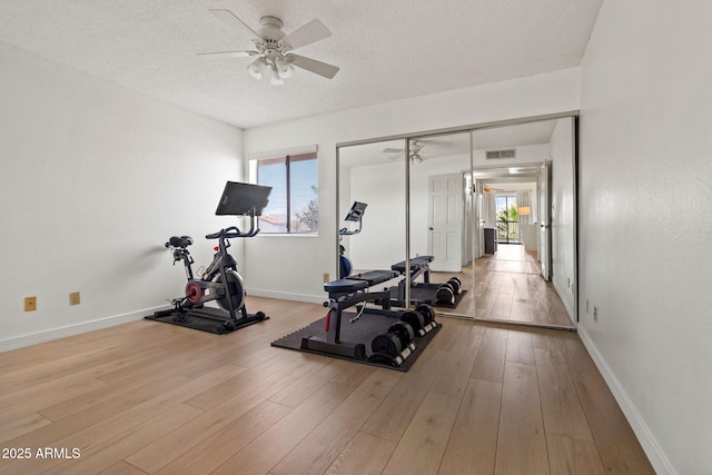 exercise room featuring ceiling fan, a textured ceiling, wood finished floors, and visible vents