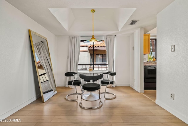 dining area with a raised ceiling, visible vents, light wood-style flooring, and baseboards