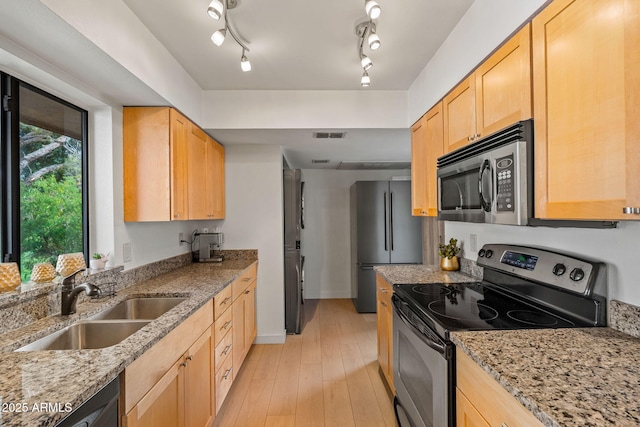 kitchen featuring freestanding refrigerator, light brown cabinetry, a sink, and stainless steel range with electric cooktop