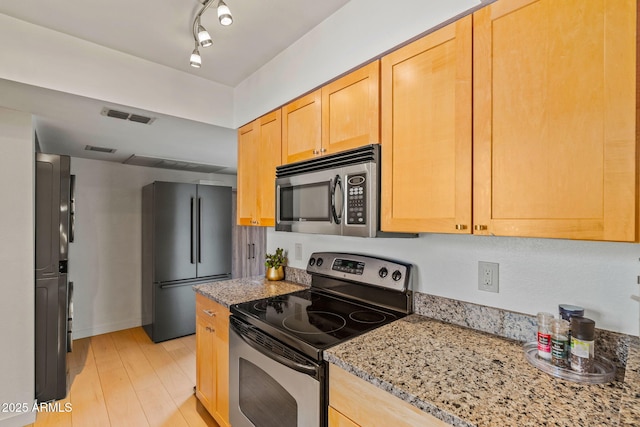 kitchen featuring appliances with stainless steel finishes, light wood-type flooring, visible vents, and light stone countertops