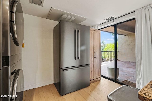 kitchen featuring light wood finished floors, stacked washer and dryer, visible vents, freestanding refrigerator, and a wall of windows