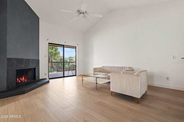 living area featuring high vaulted ceiling, a tiled fireplace, wood finished floors, and a ceiling fan