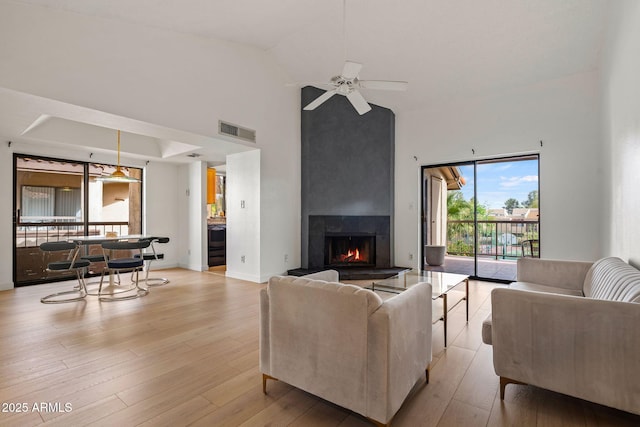 living room with light wood finished floors, a large fireplace, visible vents, a ceiling fan, and high vaulted ceiling