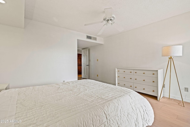 bedroom featuring visible vents, light wood-style floors, ceiling fan, a textured ceiling, and baseboards