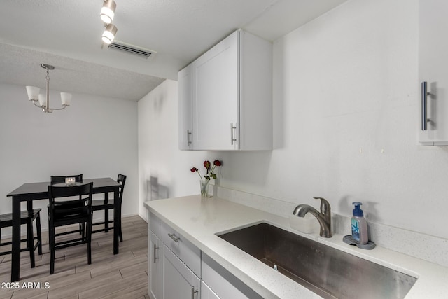 kitchen with light countertops, a sink, decorative light fixtures, and white cabinetry