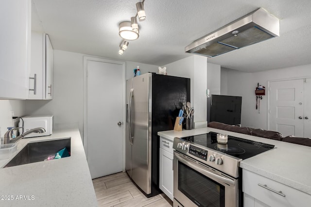 kitchen with appliances with stainless steel finishes, open floor plan, range hood, light countertops, and a sink