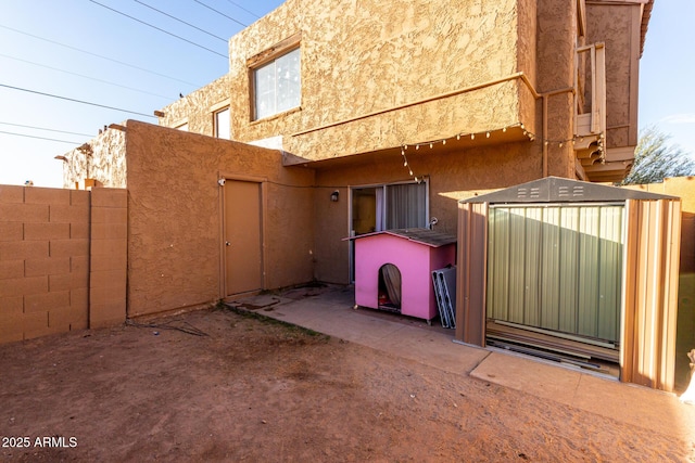 view of side of home with a shed, an outdoor structure, fence, and stucco siding