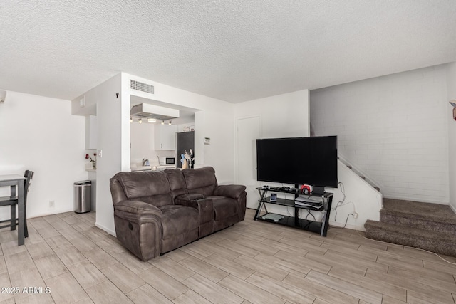 living room with wood tiled floor, stairs, visible vents, and a textured ceiling