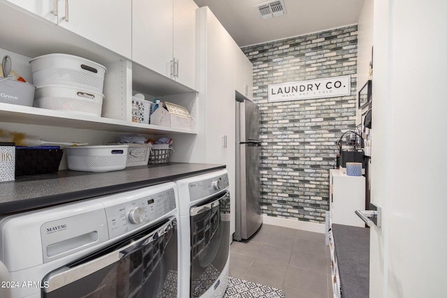 laundry room featuring visible vents, tile patterned flooring, washing machine and dryer, brick wall, and cabinet space