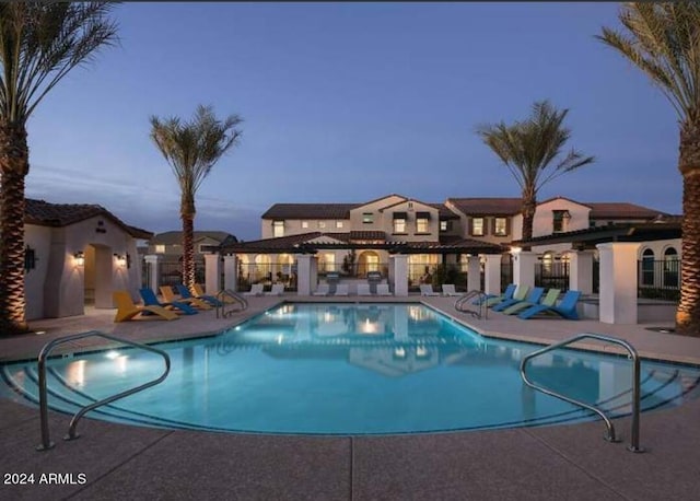 pool at dusk featuring a patio and a community pool