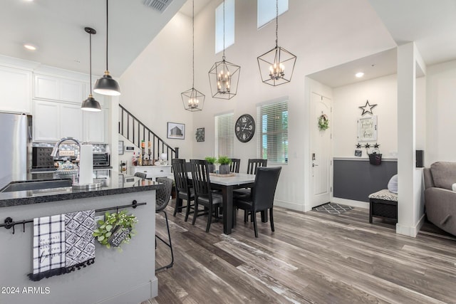 dining space featuring visible vents, stairs, a towering ceiling, dark wood-style floors, and a chandelier