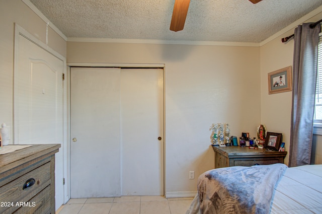 tiled bedroom with ceiling fan, a closet, a textured ceiling, and ornamental molding