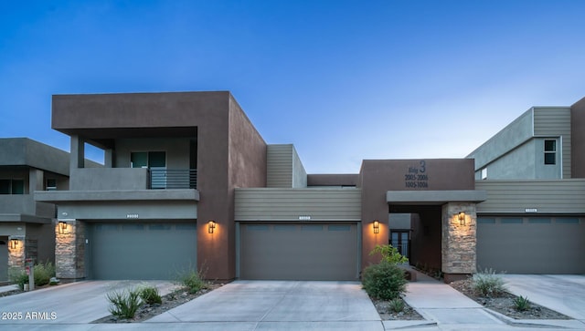 view of front of property featuring driveway, stone siding, a garage, and stucco siding