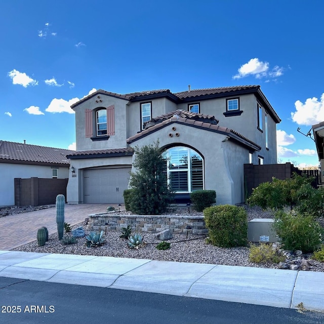 mediterranean / spanish-style home featuring decorative driveway, a tile roof, stucco siding, fence, and a garage