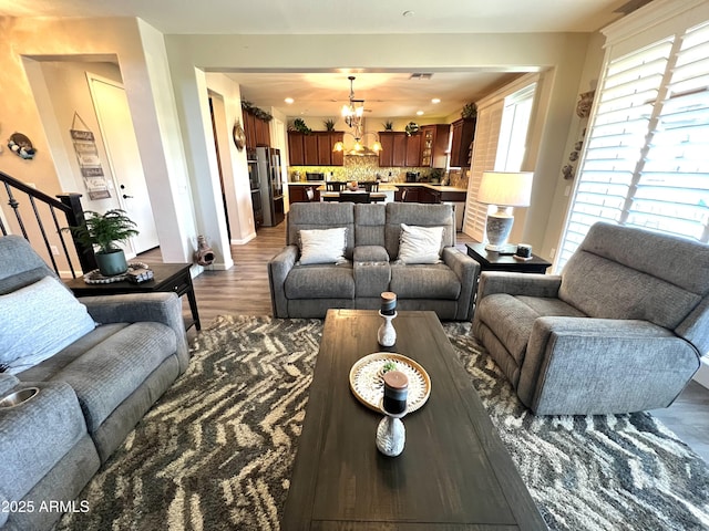 living area featuring a notable chandelier, visible vents, stairway, dark wood-type flooring, and baseboards