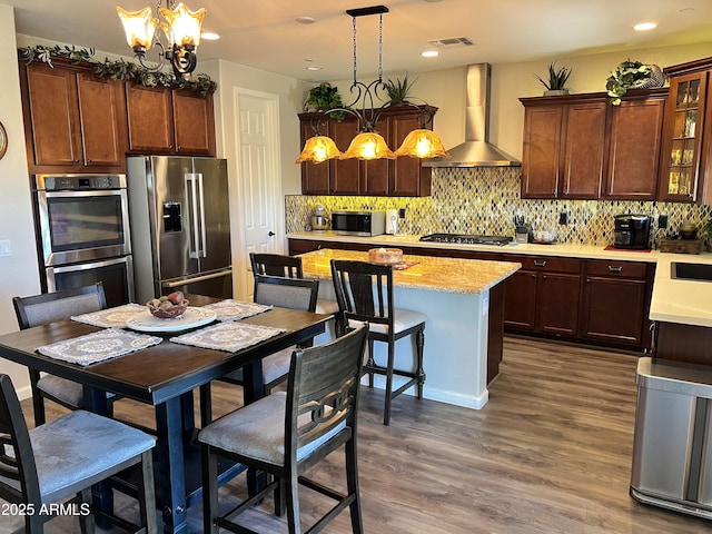 kitchen with a kitchen island, appliances with stainless steel finishes, decorative backsplash, wall chimney exhaust hood, and dark wood finished floors