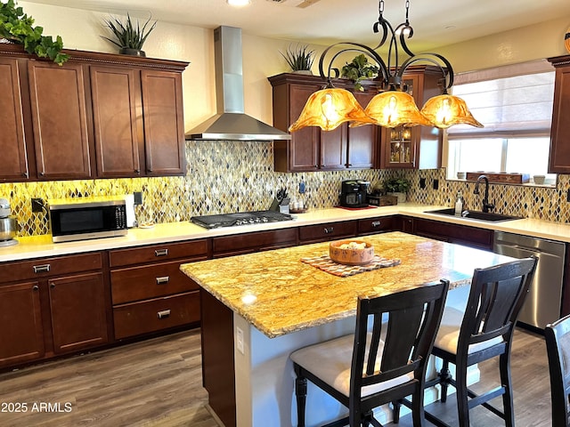 kitchen with decorative backsplash, wall chimney exhaust hood, a kitchen breakfast bar, stainless steel appliances, and a sink