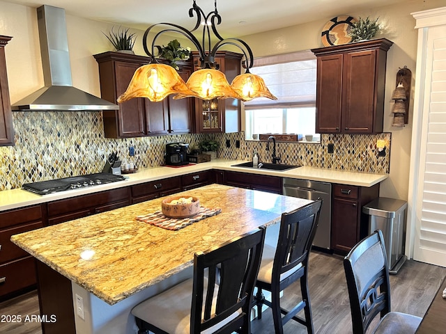 kitchen with sink, appliances with stainless steel finishes, a center island, decorative light fixtures, and wall chimney exhaust hood