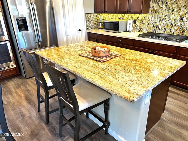 kitchen with dark brown cabinets, appliances with stainless steel finishes, a kitchen breakfast bar, a kitchen island, and light stone countertops