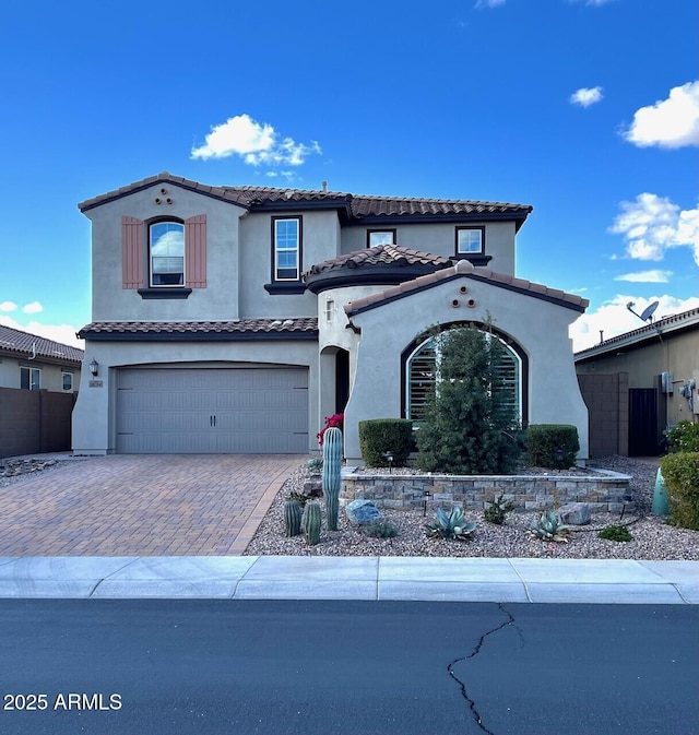 mediterranean / spanish home featuring a garage, decorative driveway, fence, and stucco siding