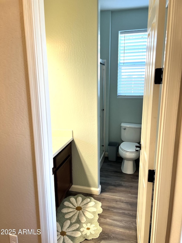 bathroom with a stall shower, baseboards, toilet, wood finished floors, and vanity