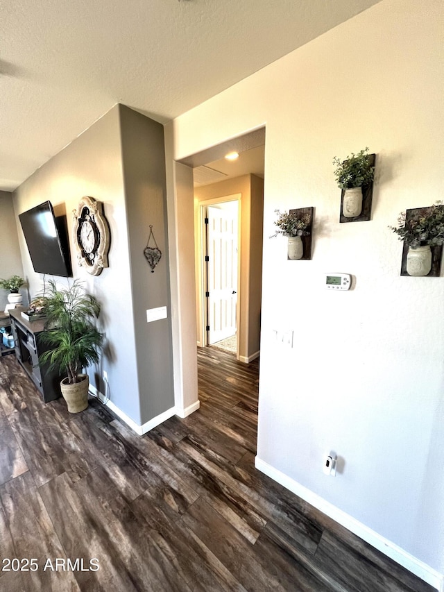 hall with a textured ceiling, baseboards, and dark wood-style flooring