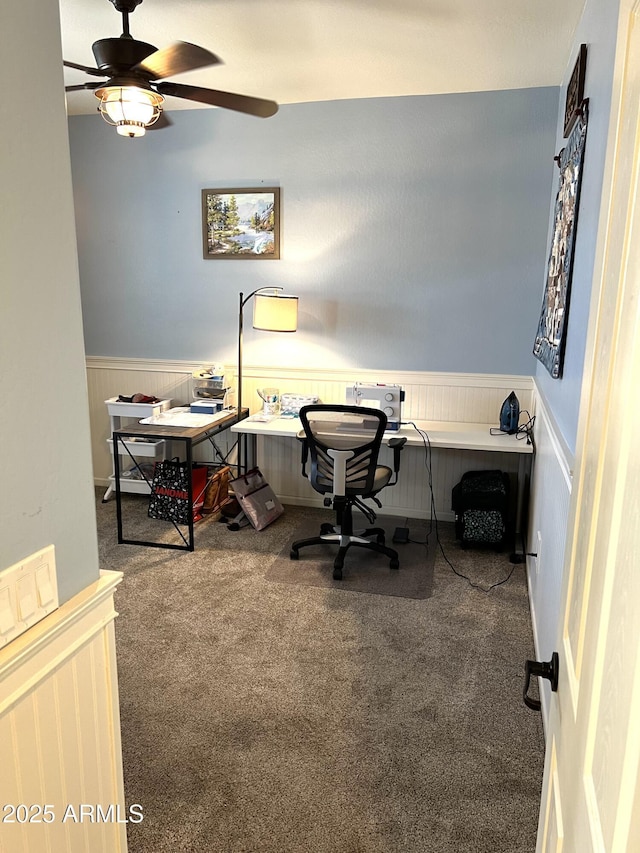 carpeted home office featuring wainscoting and a ceiling fan