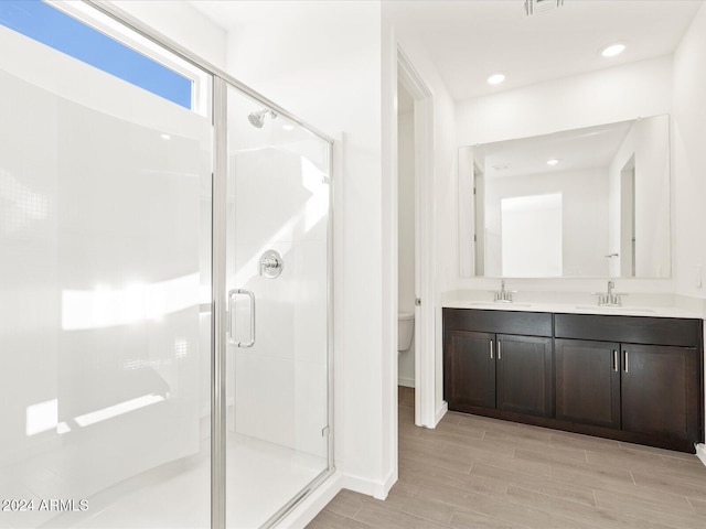 bathroom with hardwood / wood-style flooring, vanity, toilet, and a shower with shower door