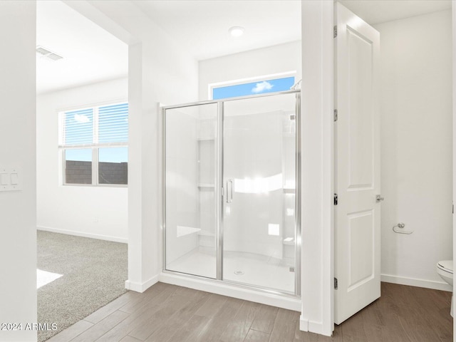 bathroom with hardwood / wood-style floors, an enclosed shower, and toilet