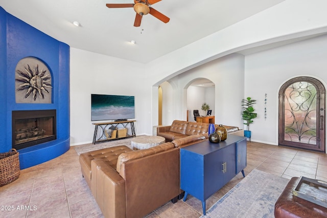 tiled living room with ceiling fan and a fireplace