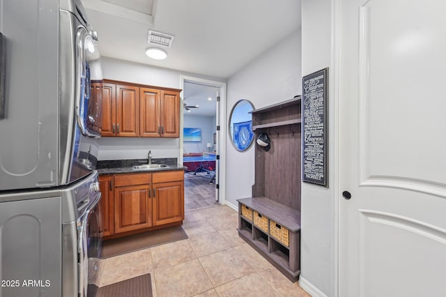 kitchen featuring stacked washer and dryer, sink, light tile patterned floors, and dark stone counters