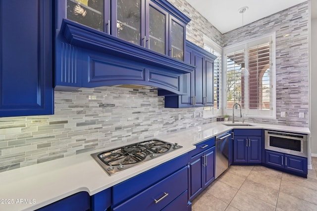 kitchen with sink, light tile patterned floors, blue cabinetry, appliances with stainless steel finishes, and backsplash