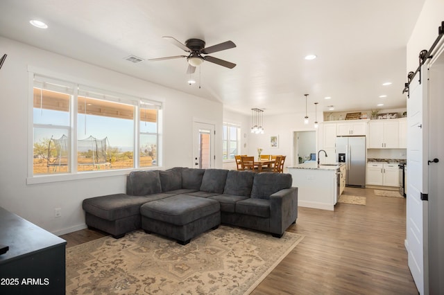 living area with visible vents, a barn door, recessed lighting, wood finished floors, and a ceiling fan