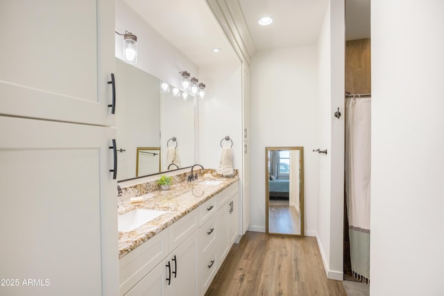 ensuite bathroom with double vanity, wood finished floors, baseboards, and a sink