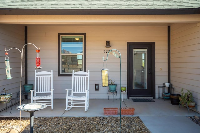 entrance to property featuring a porch and a shingled roof