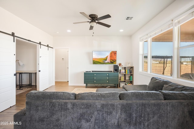living area featuring visible vents, ceiling fan, a barn door, baseboards, and wood finished floors