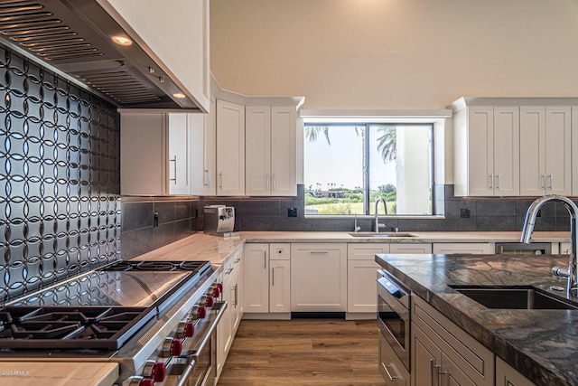 kitchen featuring appliances with stainless steel finishes, white cabinets, a sink, and wall chimney range hood