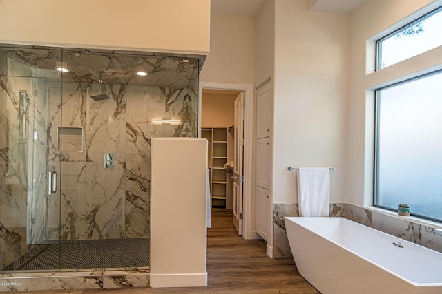 full bathroom with a soaking tub, a spacious closet, a marble finish shower, and wood finished floors