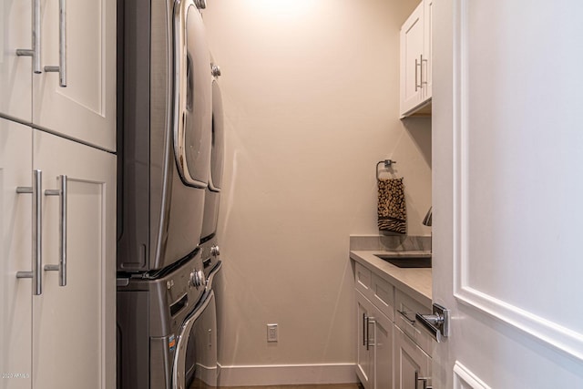 clothes washing area featuring stacked washer and clothes dryer, cabinet space, a sink, and baseboards