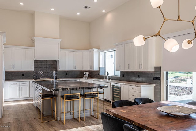 kitchen with a breakfast bar, a towering ceiling, light wood-style floors, an island with sink, and beverage cooler