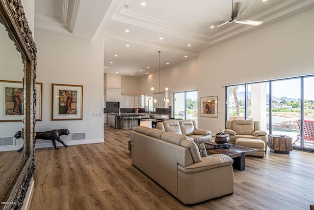 living area featuring recessed lighting, wood finished floors, a towering ceiling, visible vents, and a tray ceiling